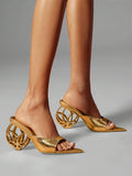Close view of gold open toe mule heels with patterned sculptural wheel heel