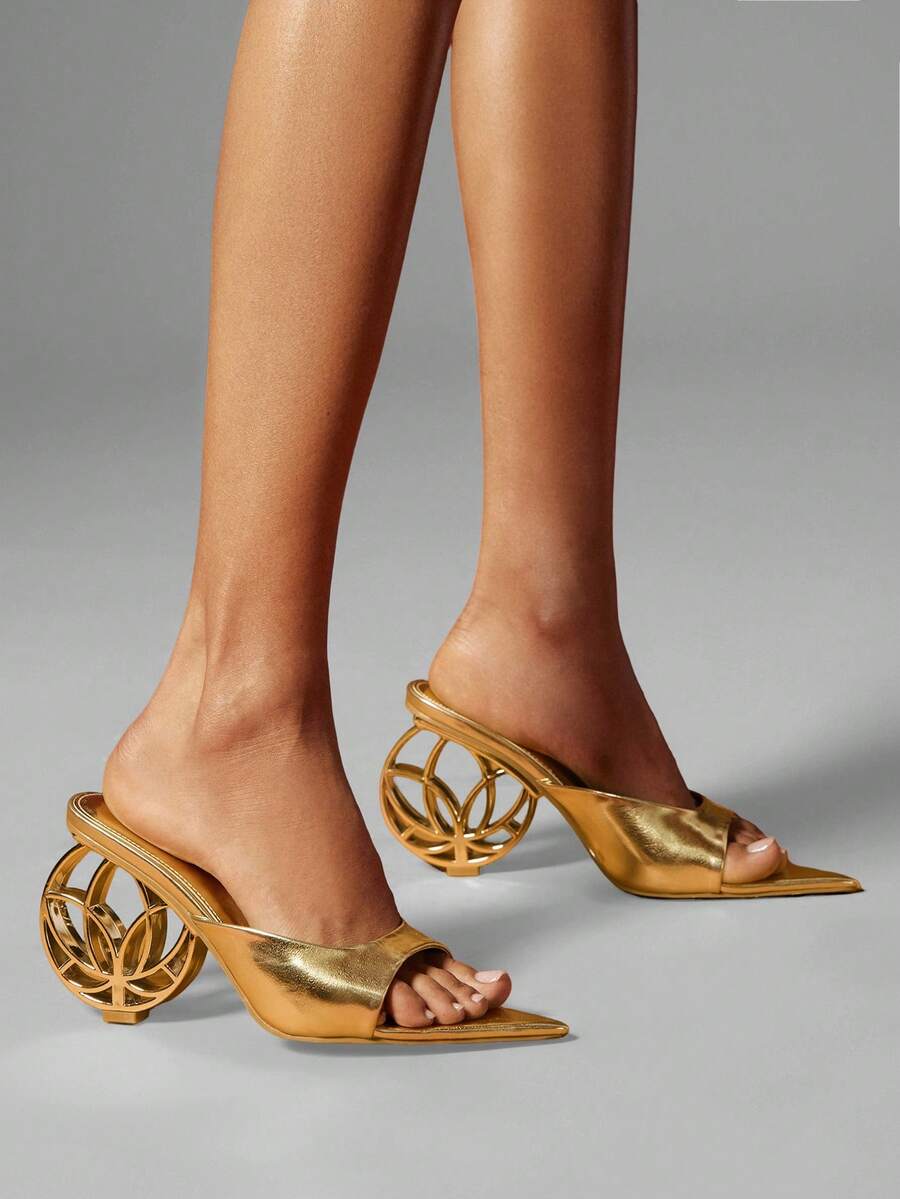 Close view of gold open toe mule heels with patterned sculptural wheel heel