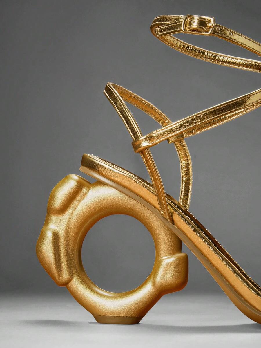 Close studio view of gold ankle strap sandals with circular gold heel detail