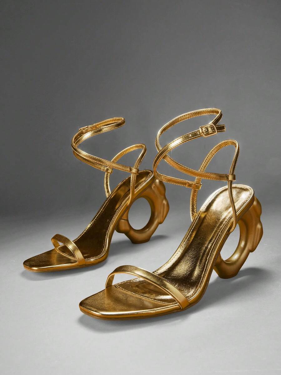 Pair of gold ankle strap sandals with circular sculptural heels in studio