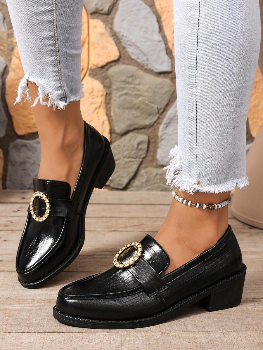 Close-up of black almond-toe loafer with gold-tone oval rhinestone buckle and low block heel