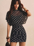 Front close view of black polka-dot mini dress with layered batwing overlay and ruched skirt