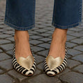 On-foot view of gold-heart zebra loafers with jeans and cobblestone background