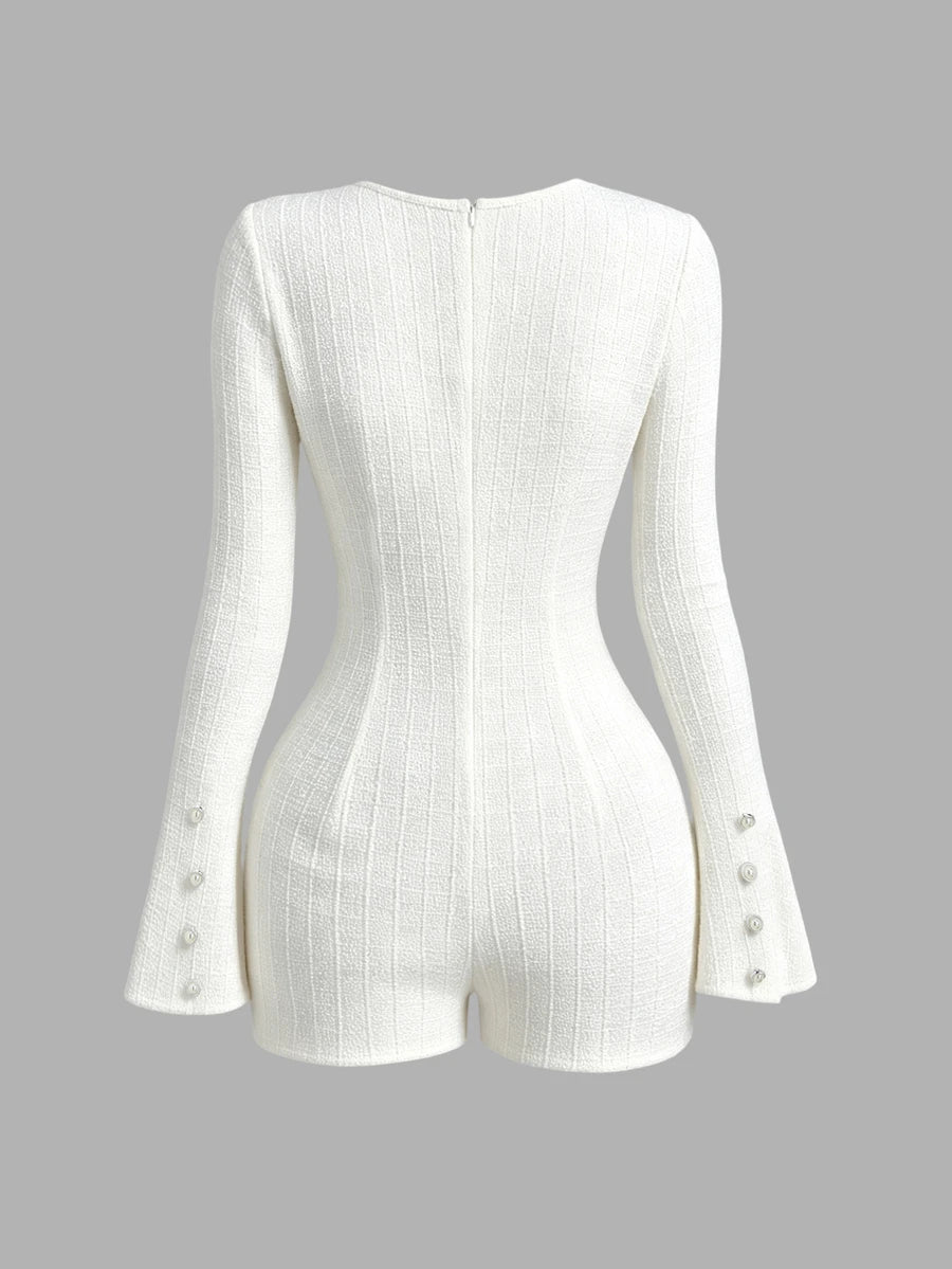 Front view of ivory textured long-sleeve romper with pearl buttons, chest pockets and flared cuffs