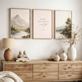 A styled interior scene showing three framed wall art prints above a wooden console table. The center print contains the text 'BE STILL, AND KNOW THAT I AM God' with a small cross above it.