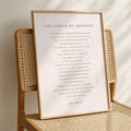 A framed scripture print featuring Psalm 23, 'The Lord is my Shepherd,' displayed on a woven rattan chair in a warm, natural setting.