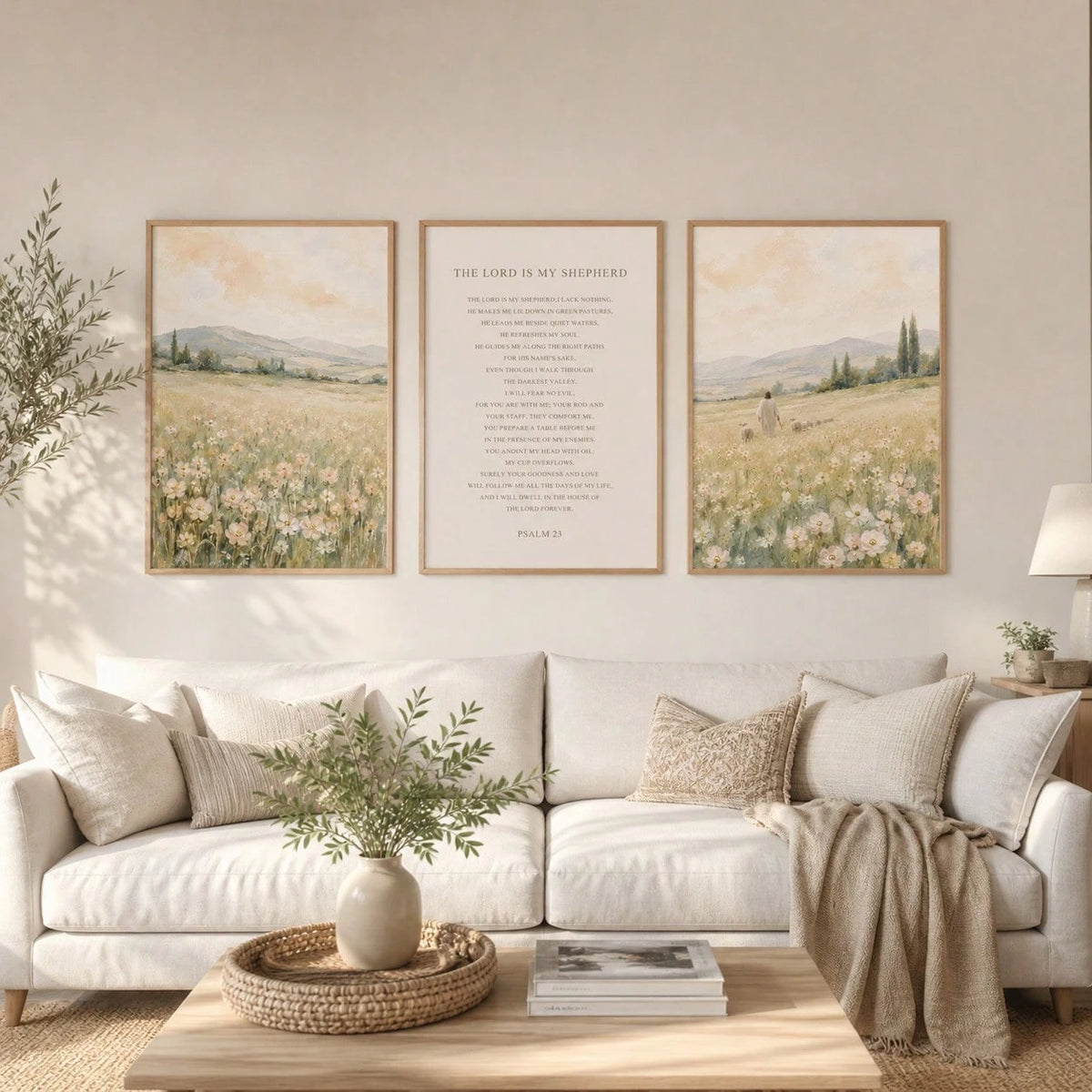 A styled living room scene with a white sofa, beige throw blanket, and a wooden coffee table. Above the sofa, three framed wall art prints are displayed: two landscape paintings showing wildflower fields and a central text print reading 'THE LORD IS MY SHEEPHER' with 'PSALM 100' below.