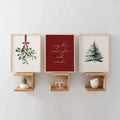 Three holiday canvas prints displayed in light frames on separate wall shelves