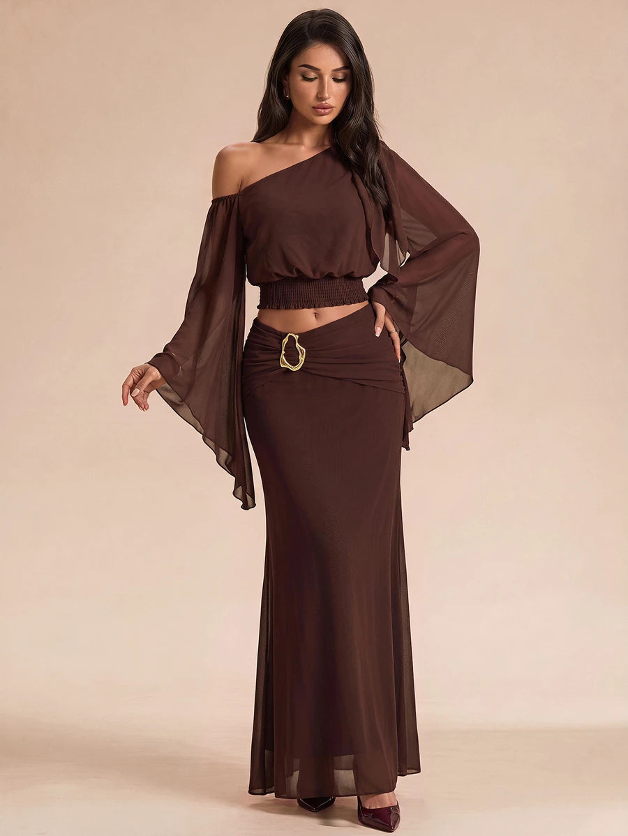 Brown asymmetrical two-piece outfit with smocked top, sheer sleeve, and flowing maxi skirt