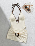 Flat lay of ivory halter swimsuit with scalloped brown trim and tortoiseshell-buckle draped skirt