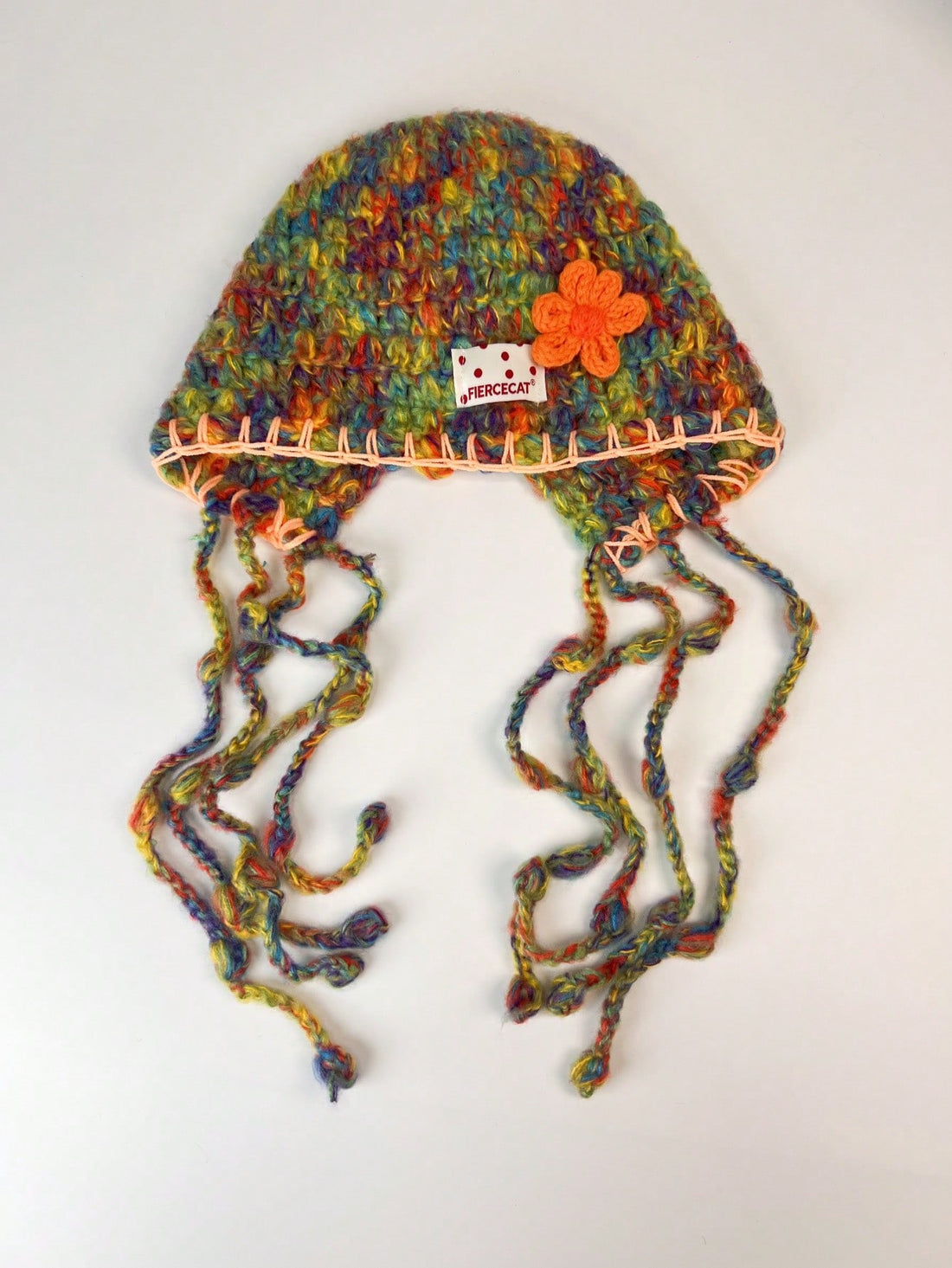 Model wearing multicolor knit earflap hat with orange flower and long braided ties