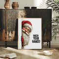 Framed Santa handwashing wall art styled on a dark cabinet among plants and neutral decor
