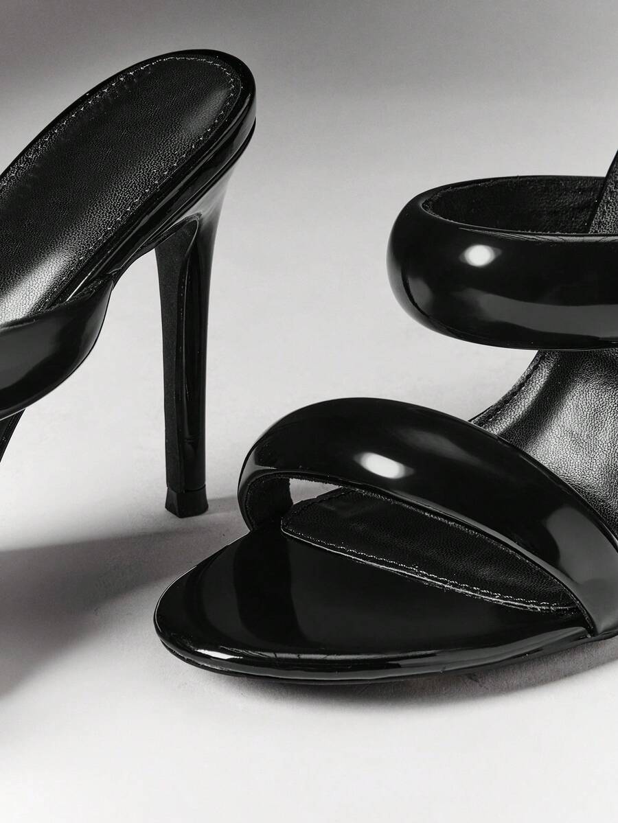 Close-up of glossy black padded straps and stiletto heel on open-toe mules