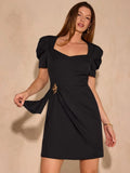 Front view of black draped mini dress with self-tie waist detail and gold-tone leaf ornament