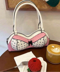 Front view of pink and white bra-shaped bow handbag with raised handles on a cafe table beside coffee