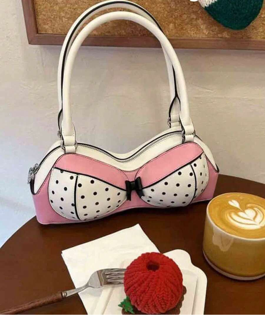 Front view of pink and white bra-shaped bow handbag with raised handles on a cafe table beside coffee