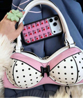 Detail view of pink and white polka-dot bra-shaped handbag showing black bow, zipper and handle rings