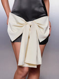 Close-up of oversized ivory bow and knot draped over the front of a black satin mini dress