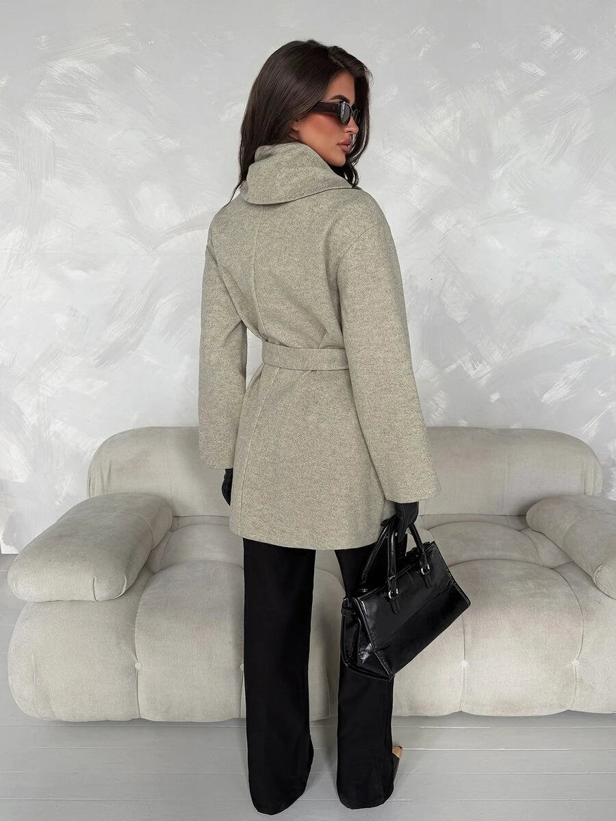 Rear three-quarter view of grey overcoat showing plain back panel, high wrap collar, waist belt and long sleeves