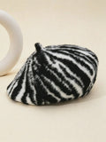 A zebra-print faux fur beret hat in black and white, styled on a warm beige background next to a white ceramic ring prop.