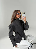 Close three-quarter view showing textured charcoal fabric, diagonal front overlap and gold-tone shoulder stud