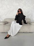 Model seated wearing dark grey asymmetric wrap jacket with tall collar and long sleeves