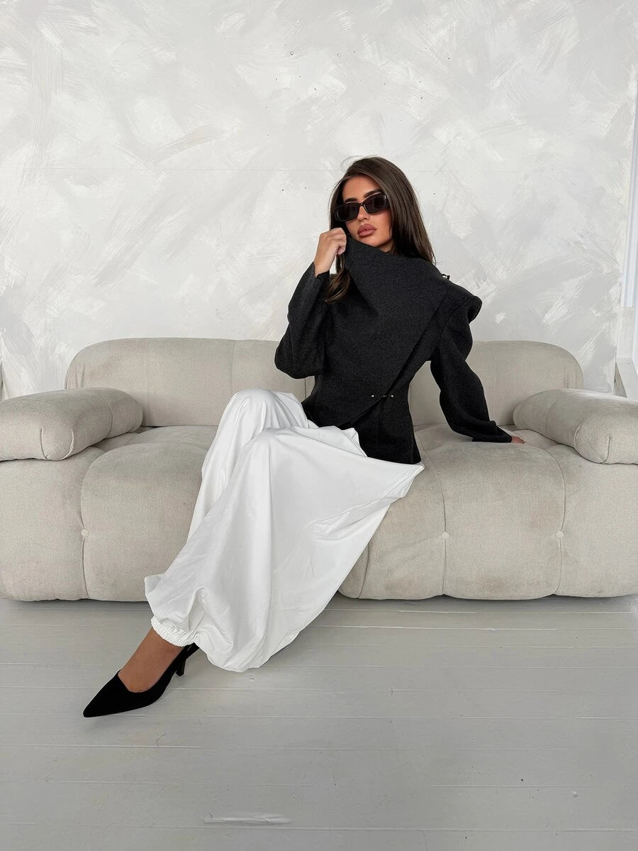 Model seated wearing dark grey asymmetric wrap jacket with tall collar and long sleeves
