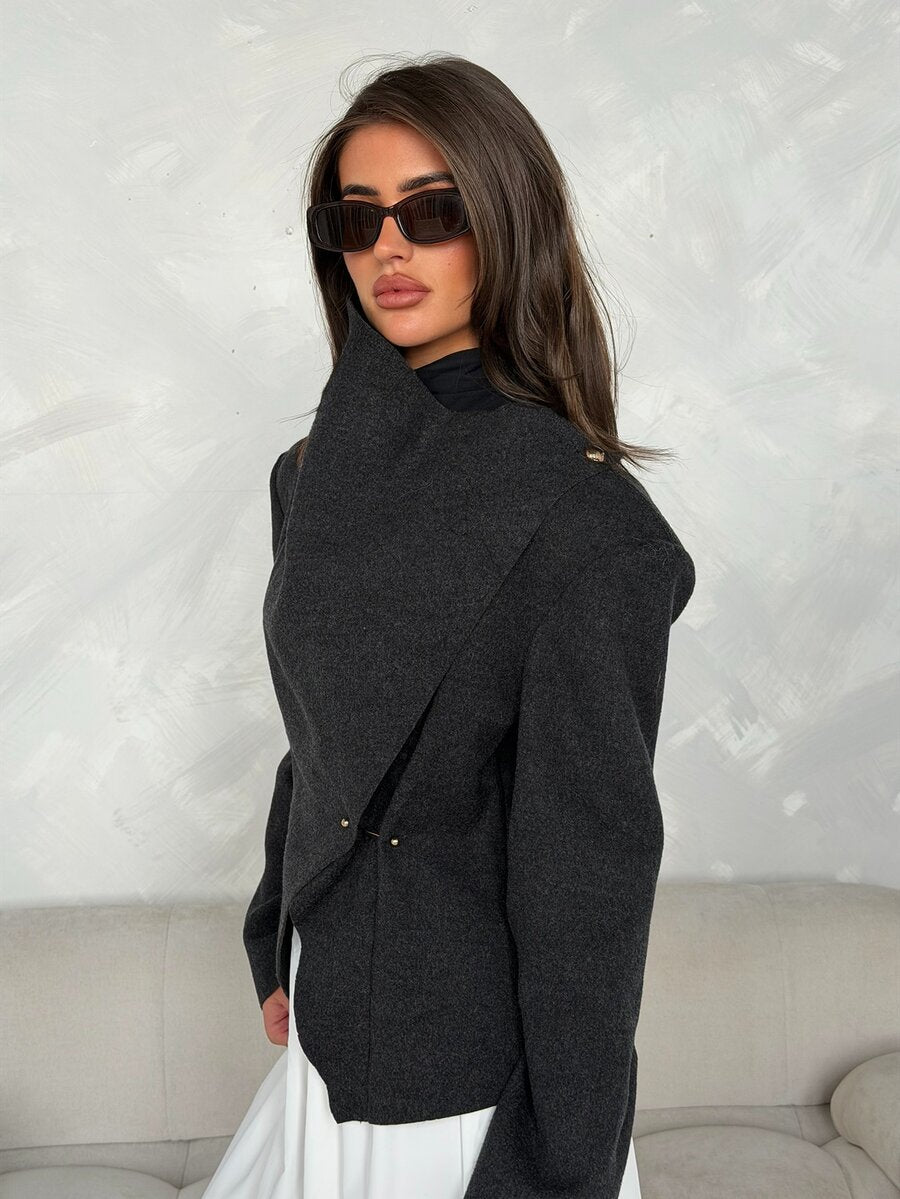 Close view of charcoal jacket high collar, angled wrap front and small gold-tone fasteners
