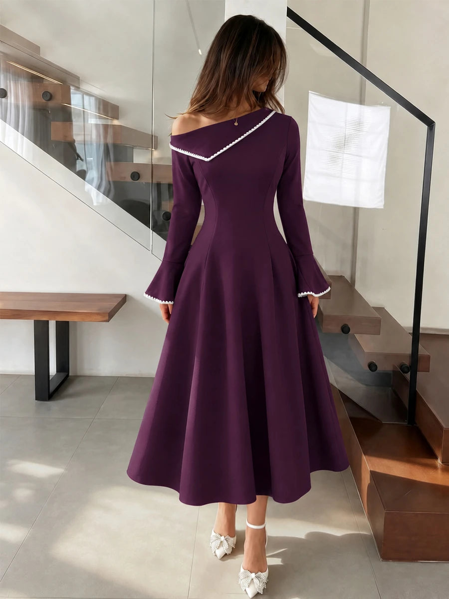 Front full-length purple dress with asymmetrical neckline, white trim and flared cuffs at stone doorway