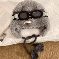Top view of gray fuzzy trapper hat with dark brown decorative goggles and braided chin ties