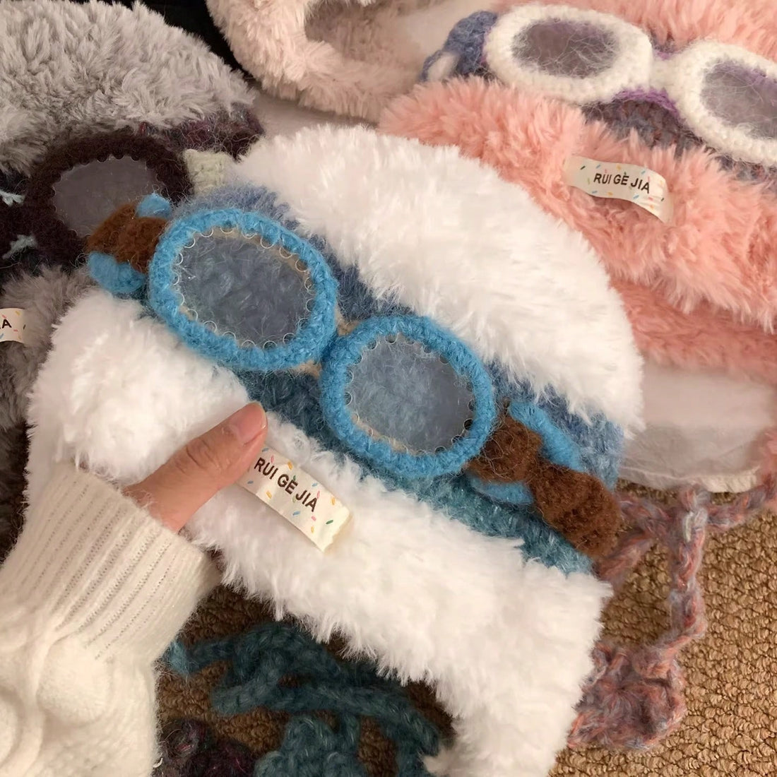 Front view of model wearing blue and brown fuzzy aviator trapper hat with white plush ear flaps and goggle motif
