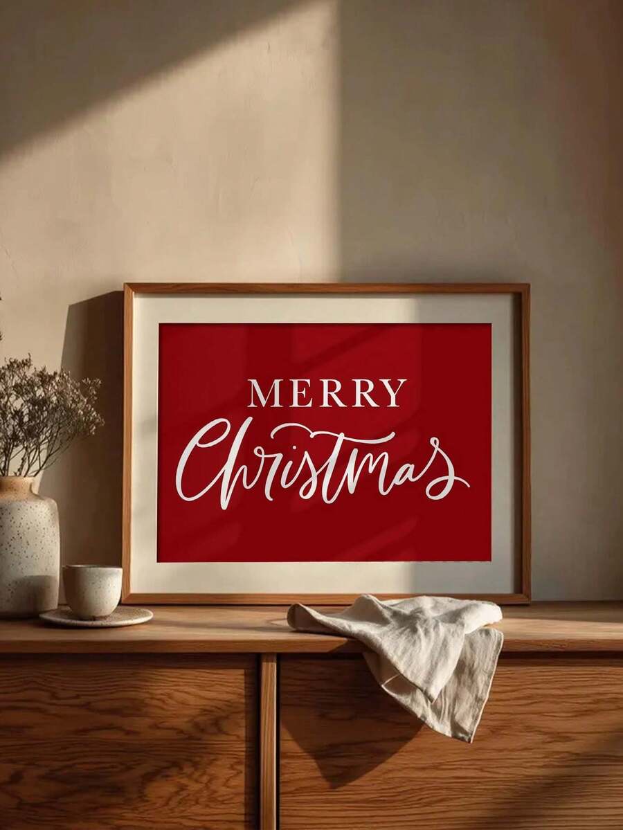 Red canvas wall art reading “MERRY Christmas” in white serif and cursive lettering, displayed in a light wood frame above a console shelf