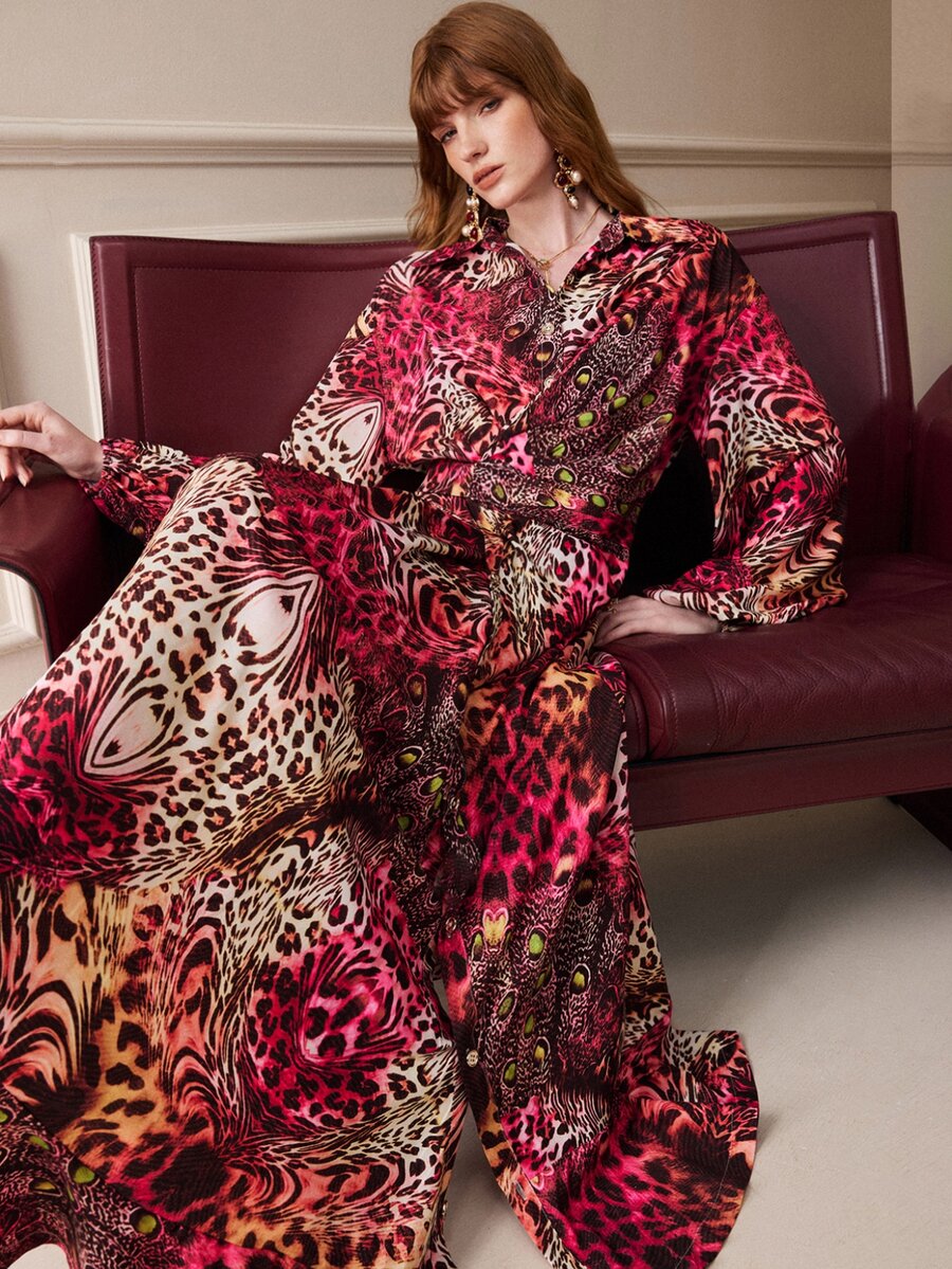 Seated view of the vivid multicolor animal-print dress showing its collared bodice and long flounce sleeves.