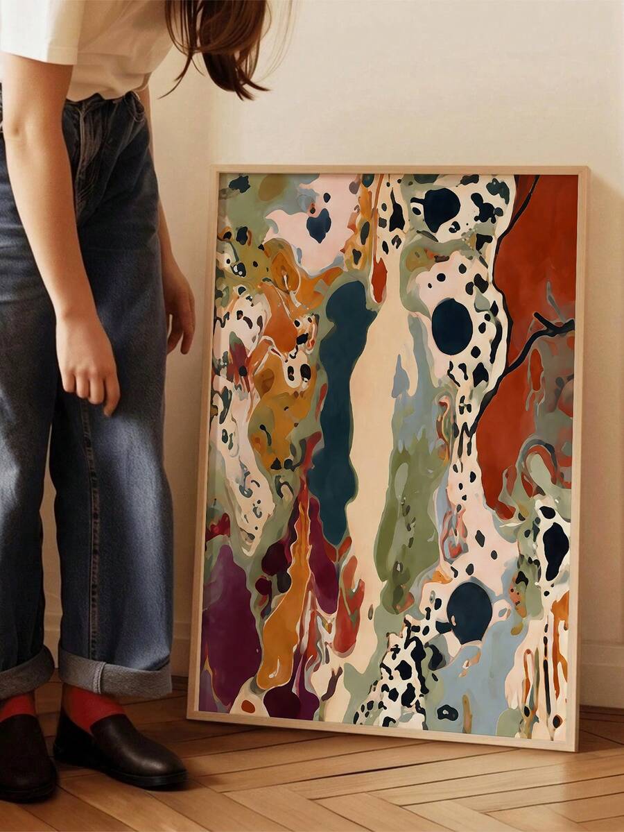 Floor-level view of a light-wood-framed abstract print with flowing multicolor shapes beside a standing person