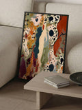 Angled close view of a dark-framed abstract canvas print leaning beside a neutral sofa and coffee table
