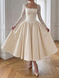 Full front view of an ivory square-neck dress with sheer lace sleeves and a voluminous ankle-length skirt indoors.