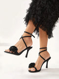 Black high-heeled sandals with floral details worn with a black ruffled skirt on a white background