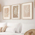 Front living room mockup of three beige botanical leaf prints in light wood-look frames above a sofa