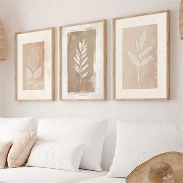 Front living room mockup of three beige botanical leaf prints in light wood-look frames above a sofa