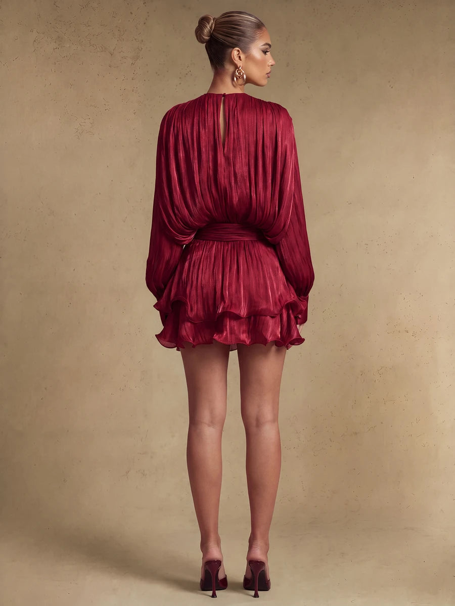 Back view of a burgundy pleated mini dress showing the gathered waist, long sleeves, and layered ruffle hem
