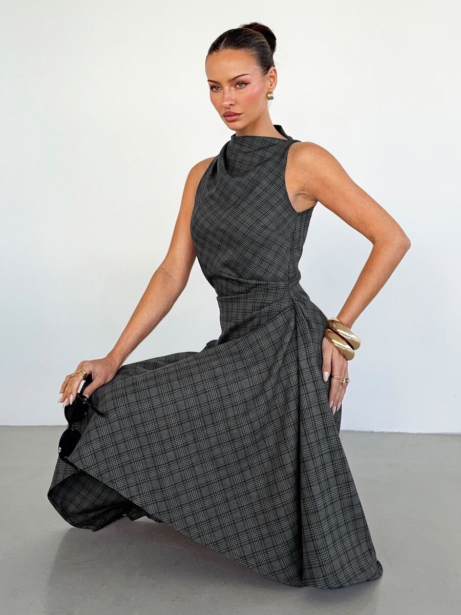 Seated view of the charcoal plaid sleeveless midi dress with its flowing asymmetric skirt displayed.