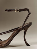 Close-up of brown patent-look ankle strap, gold-tone buckle and stiletto heel detail