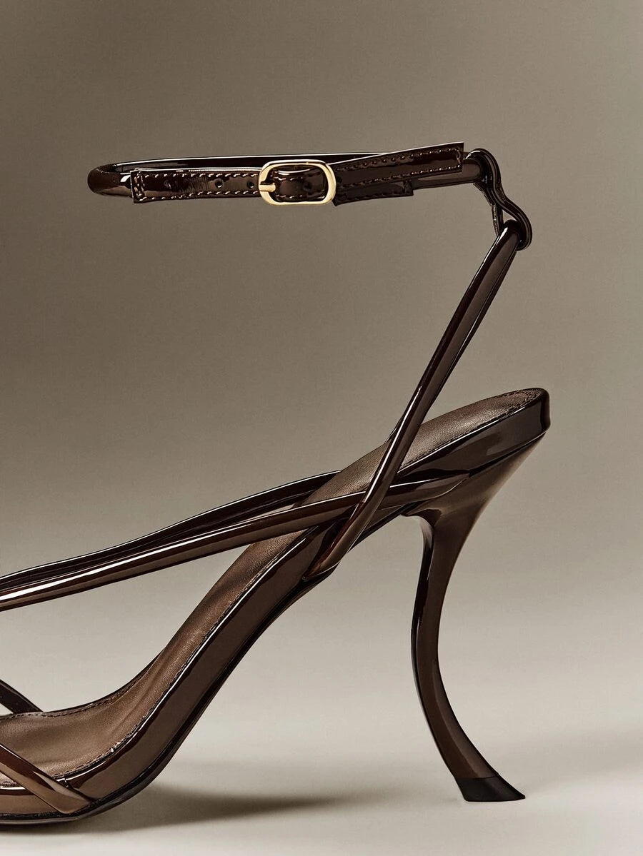 Close-up of brown patent-look ankle strap, gold-tone buckle and stiletto heel detail