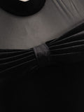 Close-up of black dress showing sheer mesh and pleated velvet-look bow at neckline