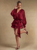 Three-quarter view of a glossy burgundy pleated mini dress with bishop sleeve, tied sash, and ruffled skirt for party styling