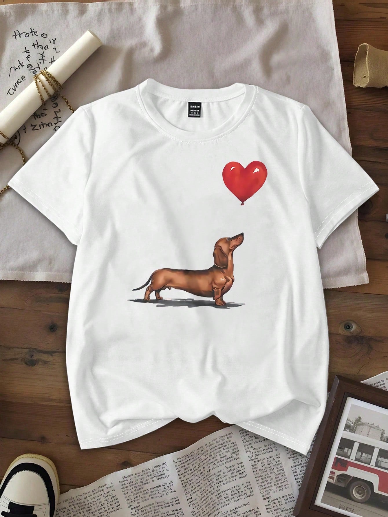 Celebrate your love for pups with this playful summer tee featuring an adorable dachshund holding a heart-shaped balloon. Lightweight and casual, it’s perfect for sunny days, adding a touch of whimsy to your outfit while keeping you comfortable and cool. Let your style wag its tail wherever you go!