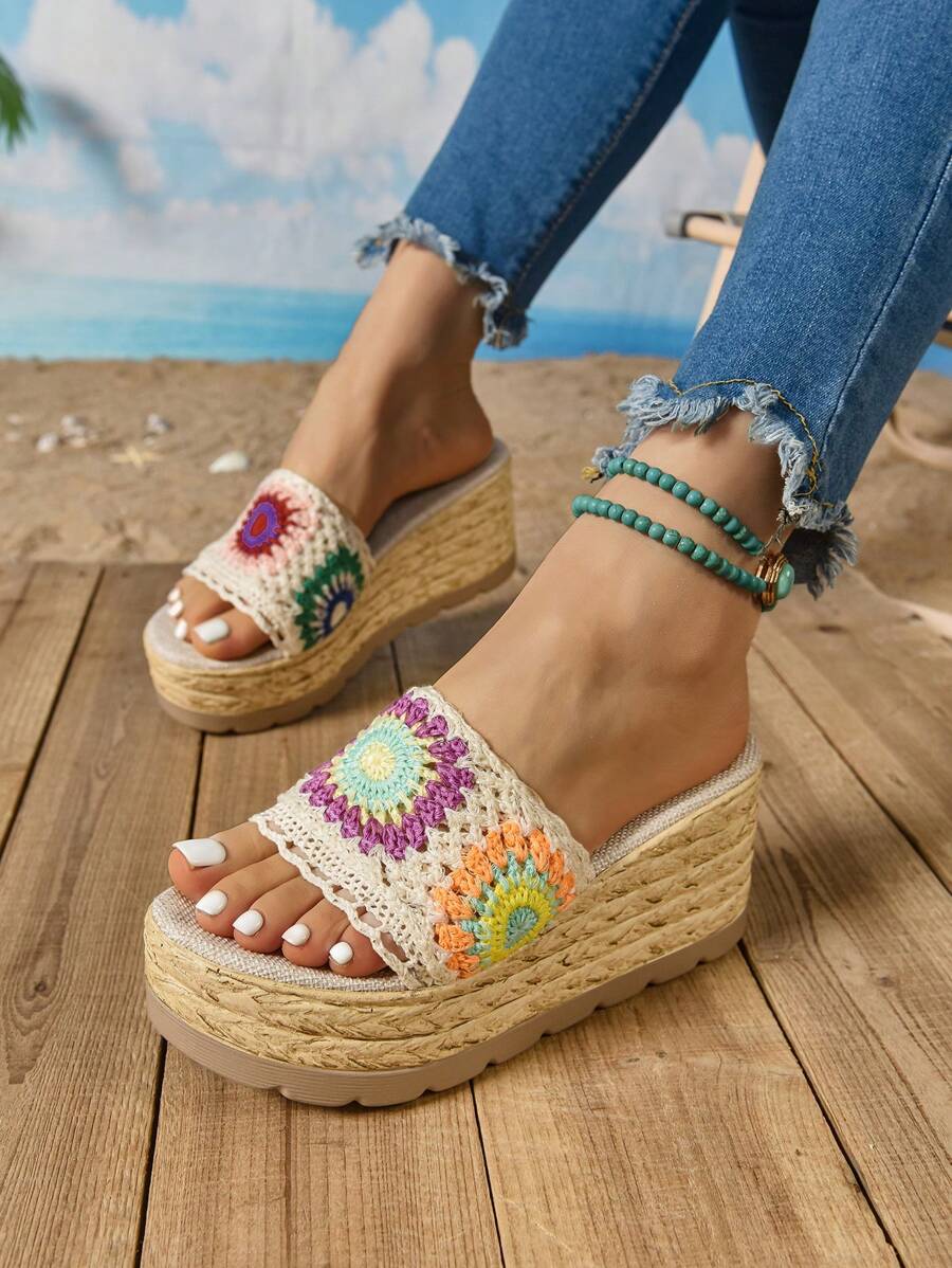 Front three-quarter view of multicolor crochet wedge slide sandals on a tropical deck