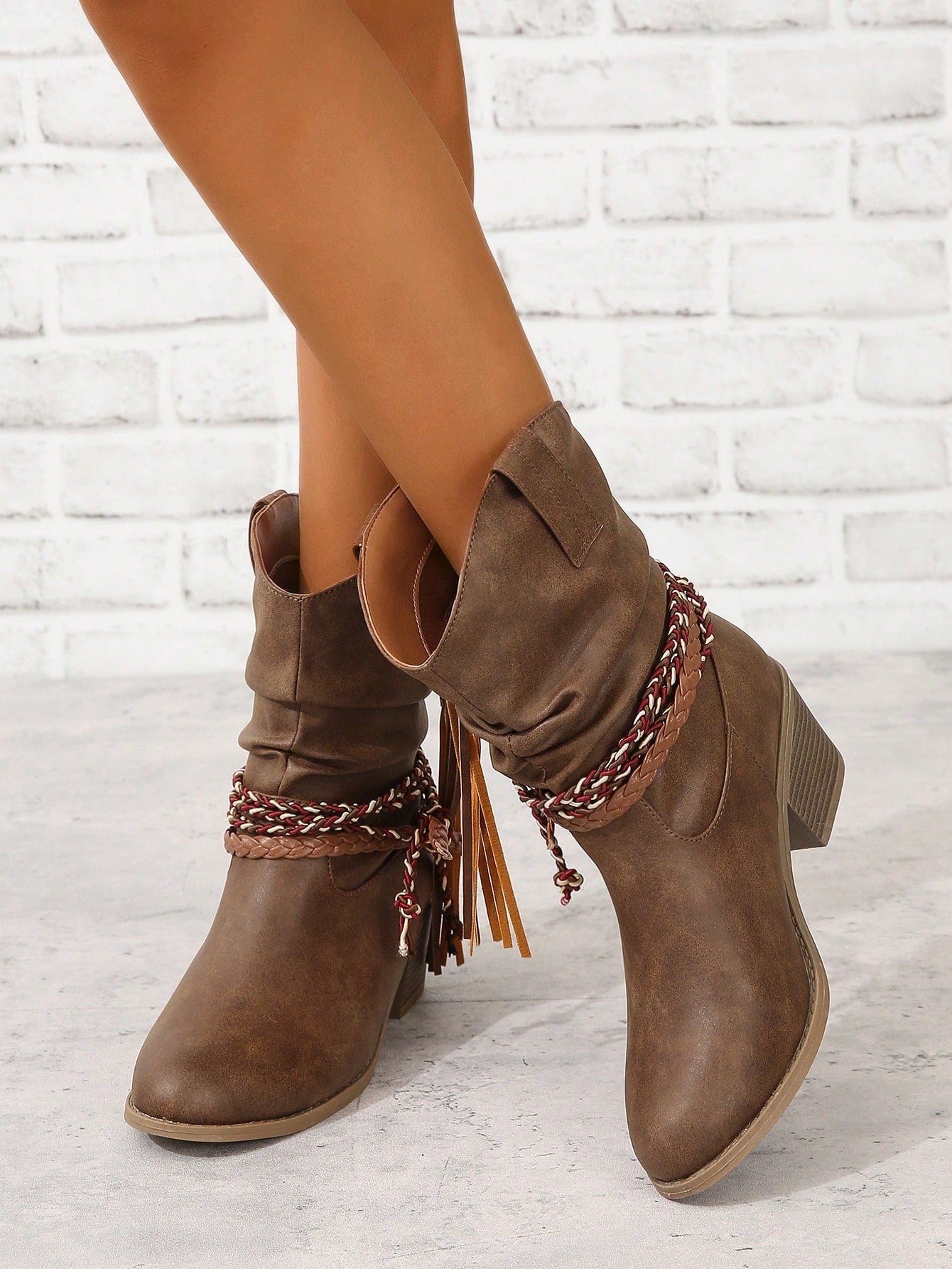 Step into bold Western-inspired style with these striking brown knee-high boots. Featuring intricate braided detailing, playful fringe accents, and functional buckle embellishments, these boots deliver serious fashion impact. The elevated heel adds confidence and elongates your silhouette, making them perfect for dressing up any outfit. Whether you're channeling cowboy chic or adding edge to casual wear, these statement boots are designed to turn heads and express your unique style.