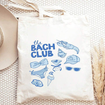 Flat lay front view of white canvas tote bag with blue The Bach Club bridal graphic