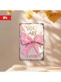 Add a charming touch to your home or café with this 'You Are Loved' Pink Bow Wall Art. The 8x12 inch decorative metal plaque features a sweet message to brighten any space. Show someone you care with this unique and playful piece of décor.
